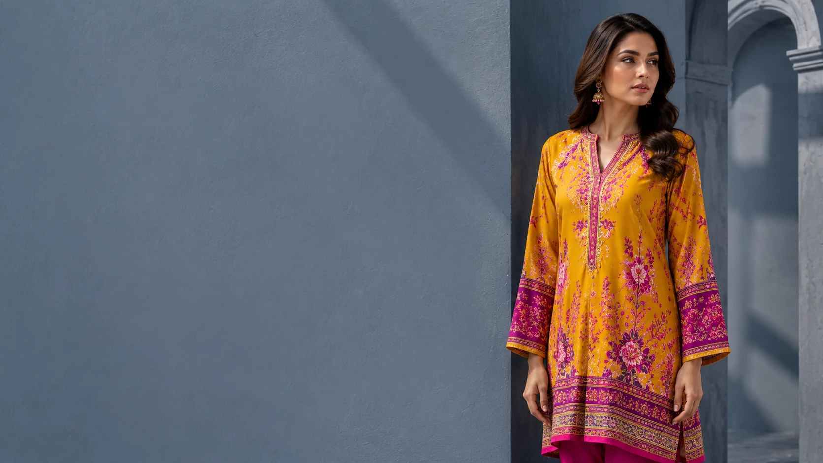 A model in a marigold and fuchsia printed kurta against a slate grey wall, from Limelight.